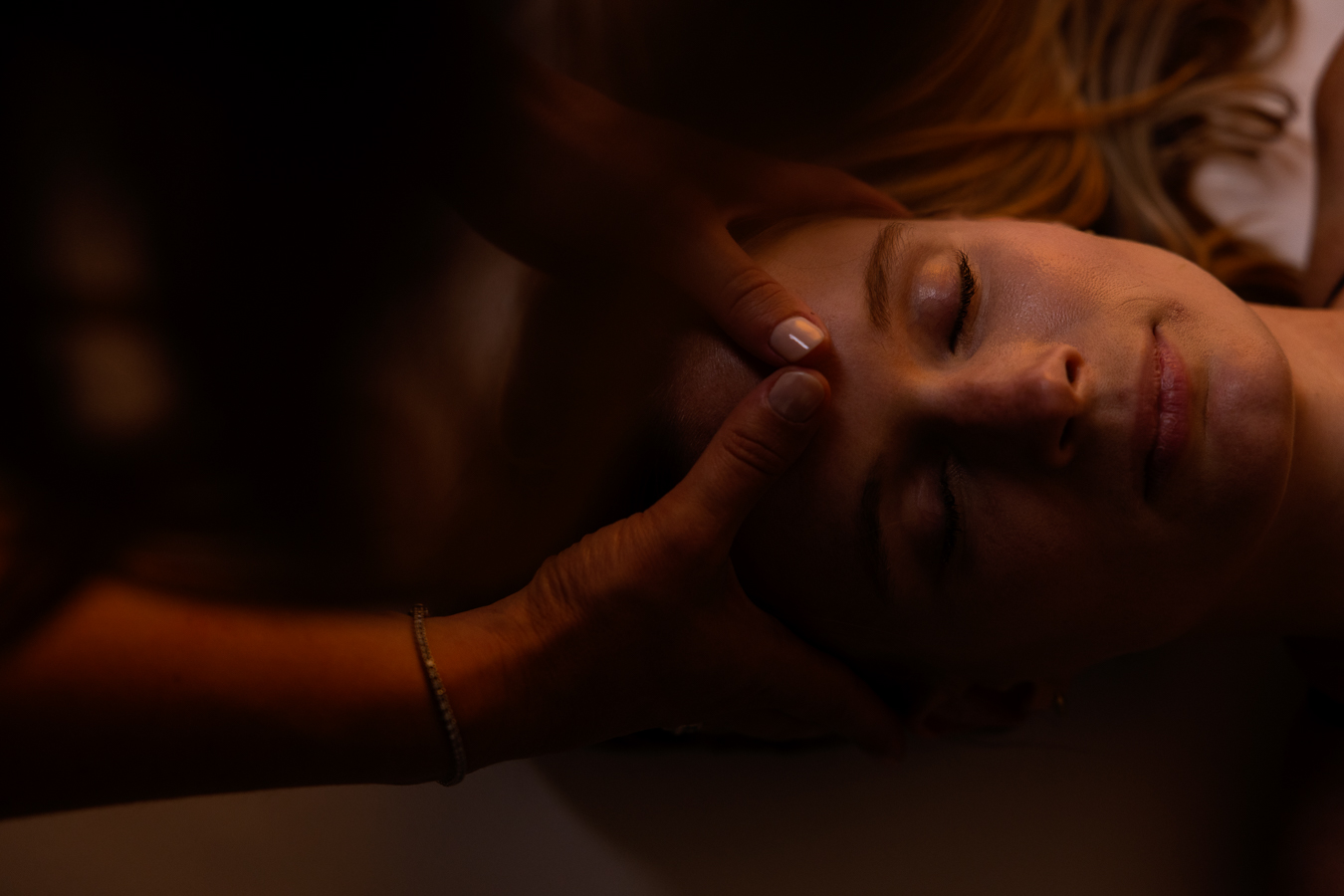 Mains soutenant le visage d'une personne allongée, lumière ambrée