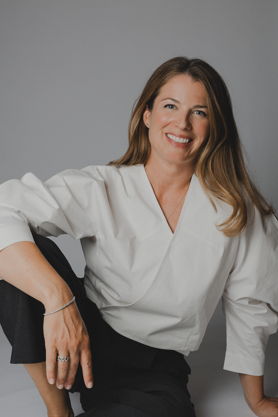 Amandine Englebert sourit, chemise blanche, sur fond gris